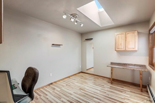 unfurnished office featuring a baseboard heating unit, light wood-type flooring, a skylight, and baseboards