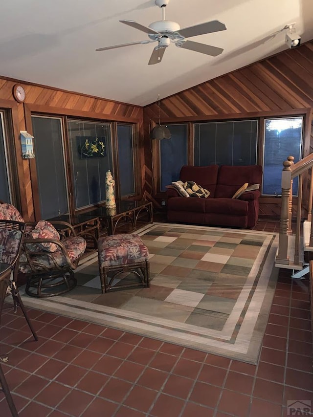 living area featuring a sunroom, ceiling fan, tile patterned floors, vaulted ceiling, and wood walls