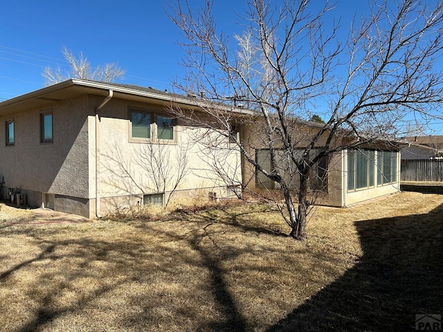 back of property featuring a yard, fence, and stucco siding