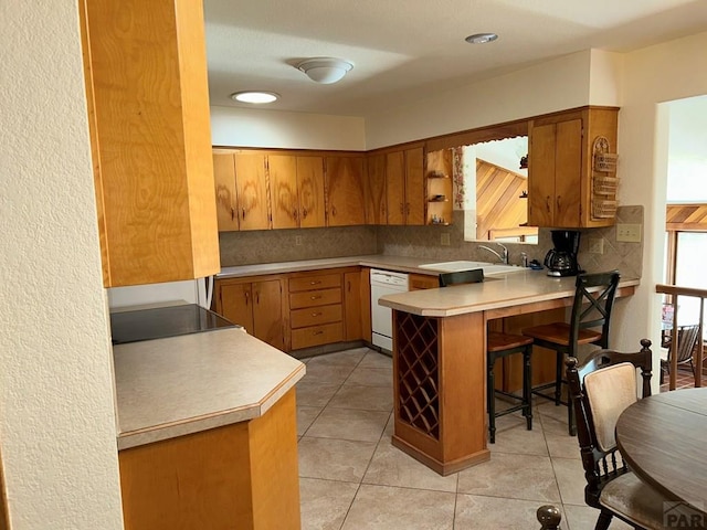 kitchen with light countertops, backsplash, a sink, dishwasher, and a peninsula