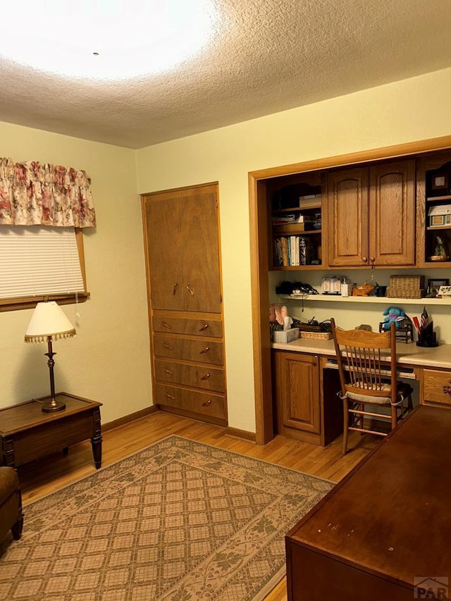 office area with light wood-style floors, a textured ceiling, baseboards, and built in desk