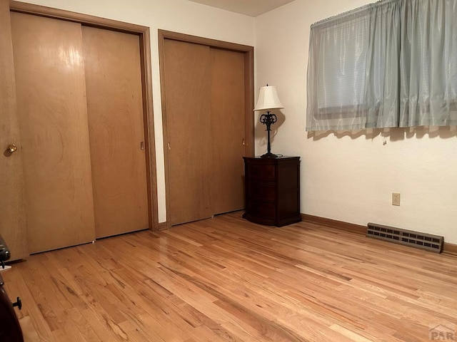 unfurnished bedroom with wood finished floors, visible vents, and two closets