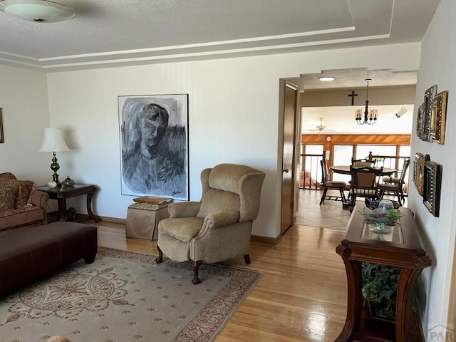 sitting room with a raised ceiling, baseboards, a notable chandelier, and light wood finished floors