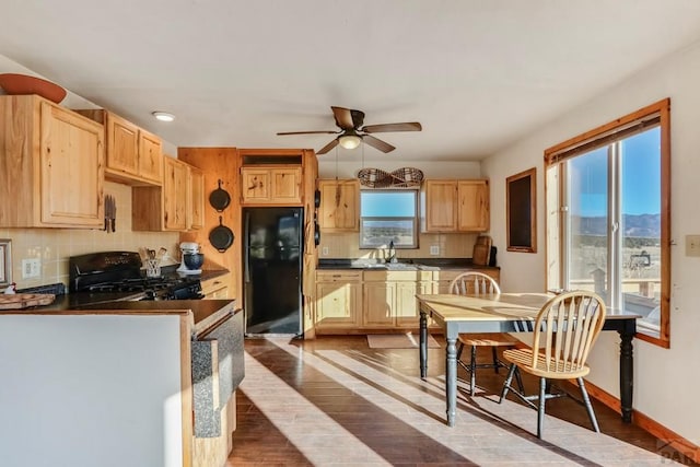 kitchen with dark wood-style floors, dark countertops, light brown cabinets, a sink, and black appliances