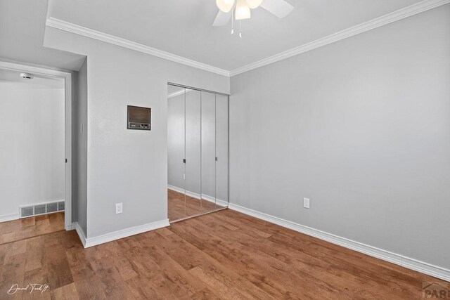 unfurnished bedroom featuring wood finished floors, visible vents, baseboards, ornamental molding, and a closet