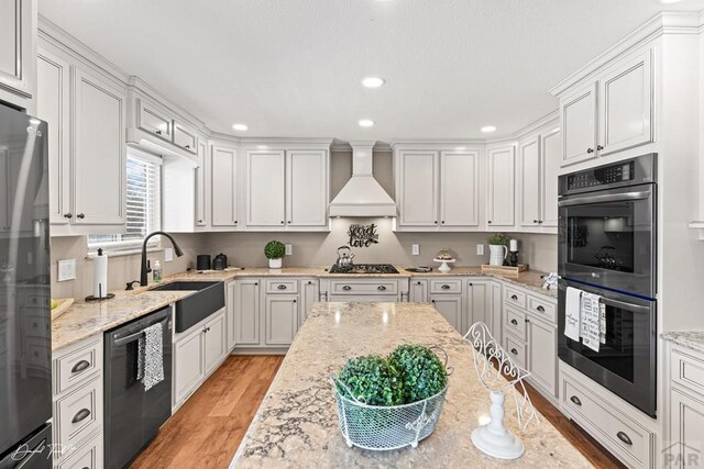 kitchen featuring custom range hood, appliances with stainless steel finishes, white cabinets, a sink, and light stone countertops