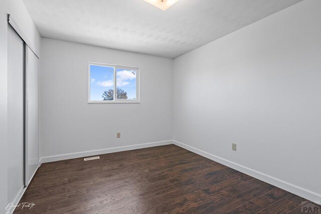 unfurnished bedroom featuring a closet, dark wood-style flooring, and baseboards