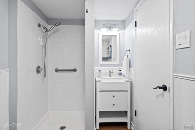 full bath featuring wainscoting, tiled shower, and vanity