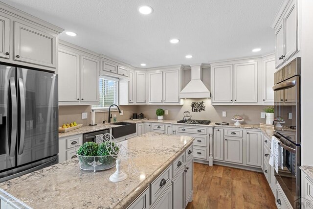 kitchen with stainless steel appliances, a sink, white cabinetry, custom exhaust hood, and light stone countertops