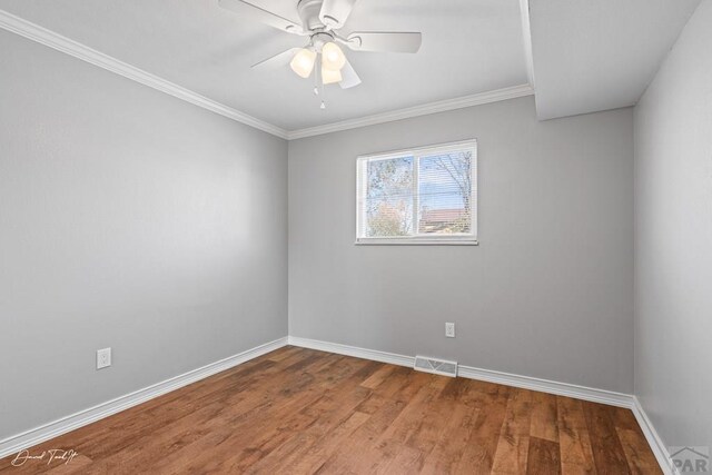 spare room with ceiling fan, wood finished floors, visible vents, baseboards, and ornamental molding