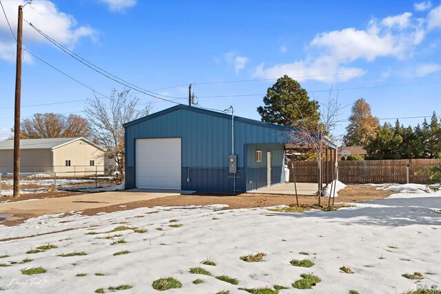 snow covered garage featuring a garage and fence