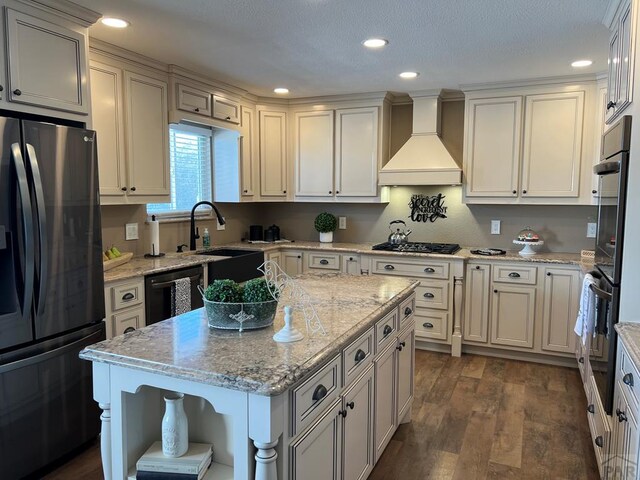 kitchen with light stone counters, a center island, dark wood-style floors, black appliances, and custom range hood