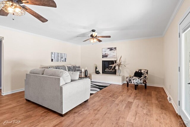 living room with ornamental molding, ceiling fan, baseboards, and wood finished floors