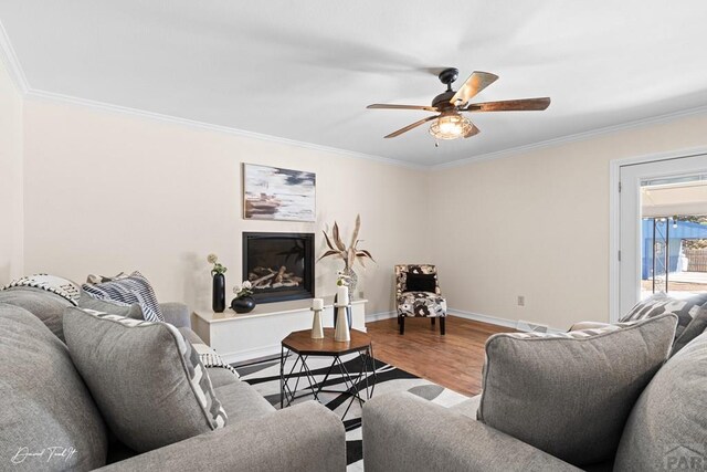 living area featuring baseboards, ceiling fan, wood finished floors, and crown molding