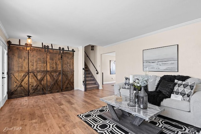 living area featuring a barn door, baseboards, wood finished floors, stairs, and crown molding