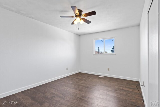 spare room featuring a ceiling fan, baseboards, and dark wood-type flooring