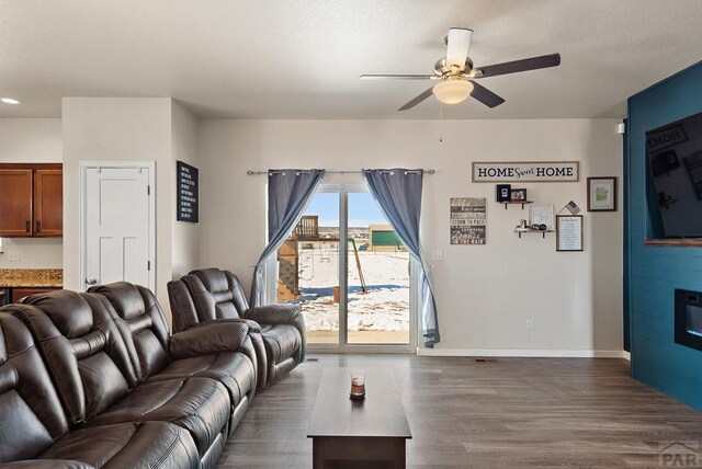 living area with dark wood-type flooring, a large fireplace, baseboards, and a ceiling fan