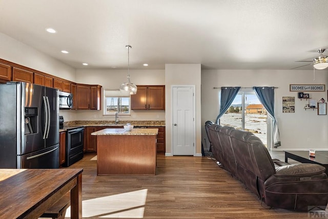 kitchen featuring a sink, a kitchen island, open floor plan, appliances with stainless steel finishes, and decorative light fixtures