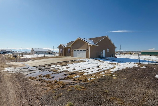 view of snowy exterior with driveway, fence, an attached garage, and stucco siding