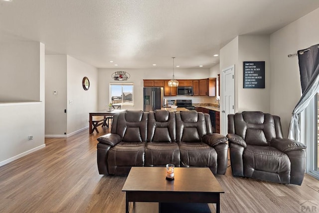 living area with light wood-style floors, recessed lighting, a textured ceiling, and baseboards