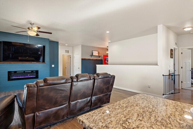 living area featuring a ceiling fan, baseboards, dark wood-type flooring, and a glass covered fireplace