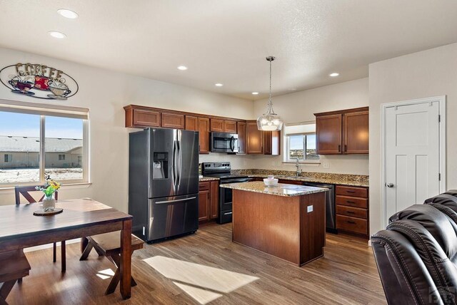 kitchen with wood finished floors, a kitchen island, appliances with stainless steel finishes, light stone countertops, and pendant lighting