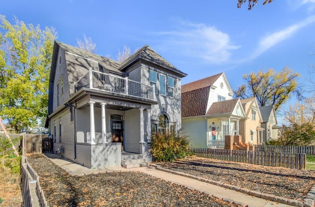 view of front facade featuring a gambrel roof, a balcony, a fenced backyard, roof with shingles, and covered porch