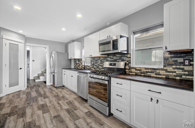 kitchen with light wood-type flooring, appliances with stainless steel finishes, white cabinets, and a sink