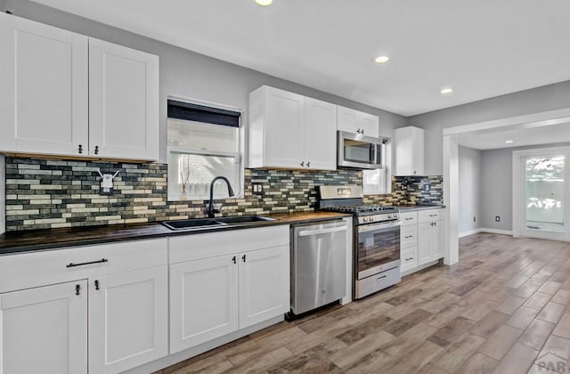 kitchen with light wood-style flooring, wood counters, a sink, white cabinets, and appliances with stainless steel finishes