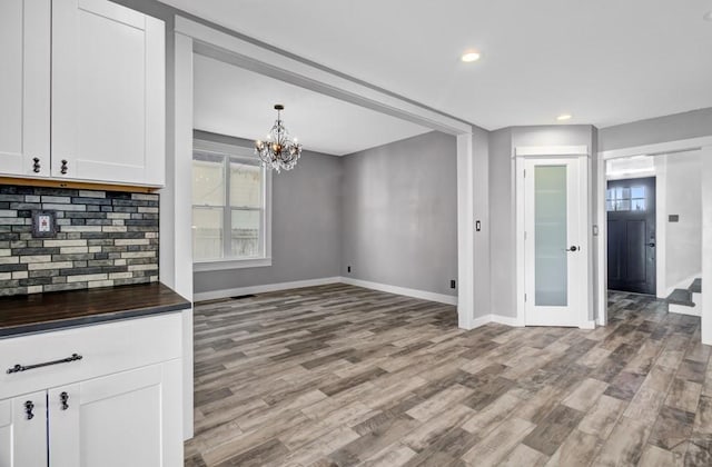 unfurnished dining area with a chandelier, light wood finished floors, recessed lighting, and baseboards