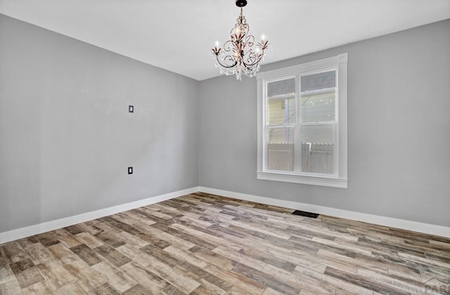 unfurnished room with light wood-style floors, baseboards, visible vents, and a notable chandelier