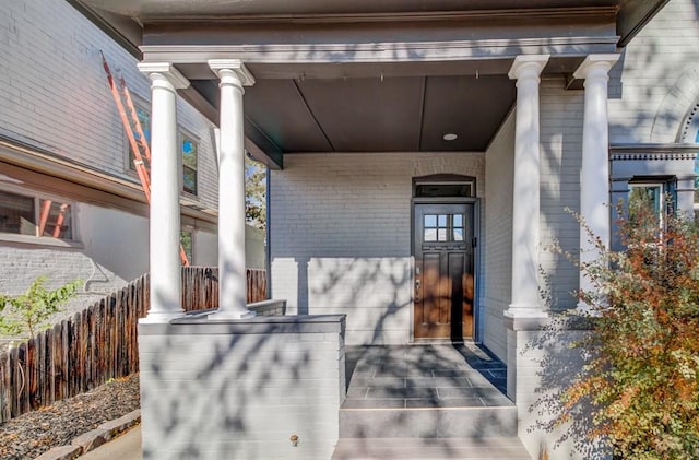 view of exterior entry featuring covered porch and brick siding