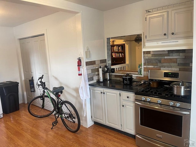 kitchen featuring light wood finished floors, tasteful backsplash, under cabinet range hood, stainless steel gas stove, and white cabinets