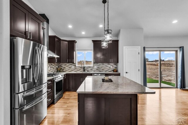 kitchen with decorative light fixtures, a center island, light stone countertops, stainless steel appliances, and a healthy amount of sunlight