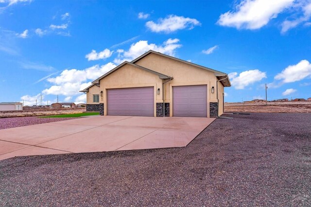 ranch-style home with an attached garage, driveway, stone siding, and stucco siding