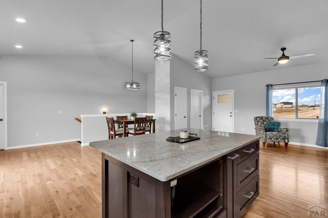 kitchen with hanging light fixtures, light wood-style floors, light stone counters, and dark brown cabinets