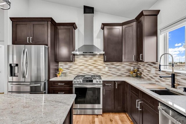 kitchen with light stone countertops, wall chimney exhaust hood, appliances with stainless steel finishes, and a sink