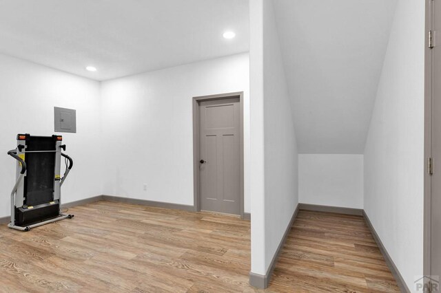 exercise room featuring light wood finished floors, electric panel, and baseboards