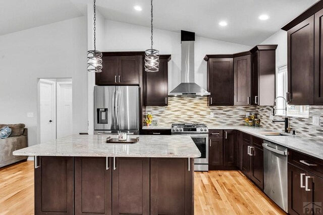 kitchen with hanging light fixtures, appliances with stainless steel finishes, a sink, wall chimney range hood, and a kitchen island