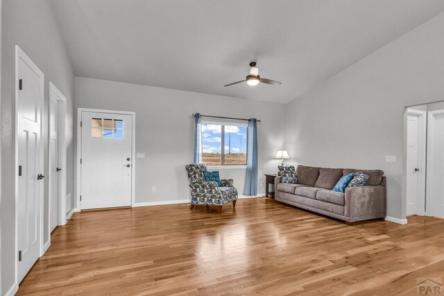 living area featuring lofted ceiling, light wood finished floors, baseboards, and a ceiling fan