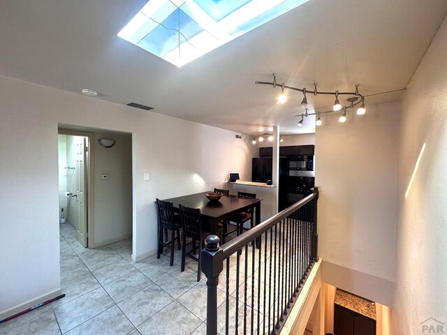 hall featuring light tile patterned floors, a skylight, visible vents, an upstairs landing, and baseboards