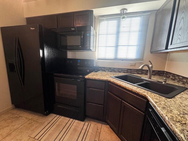 kitchen featuring light tile patterned floors, a sink, dark brown cabinets, light stone countertops, and black appliances