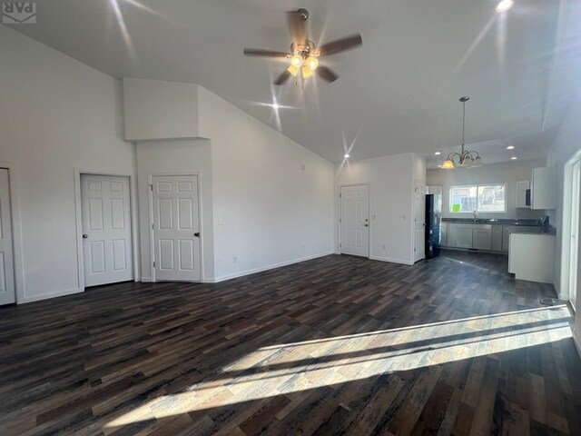 unfurnished living room featuring a sink, baseboards, dark wood-type flooring, and ceiling fan with notable chandelier