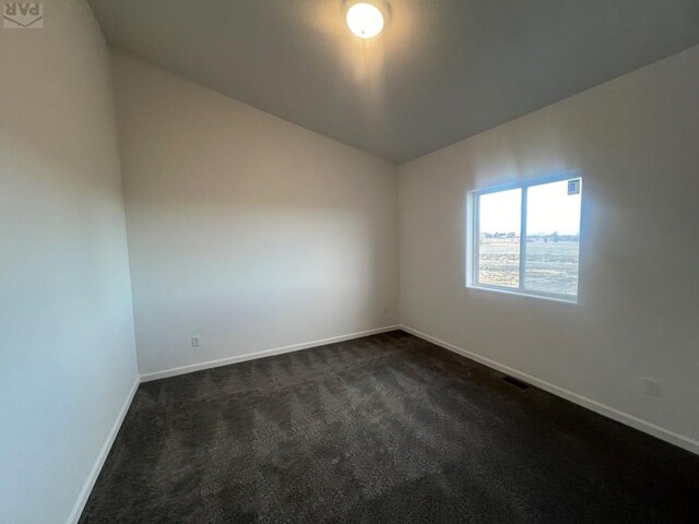 empty room featuring lofted ceiling, dark colored carpet, visible vents, and baseboards