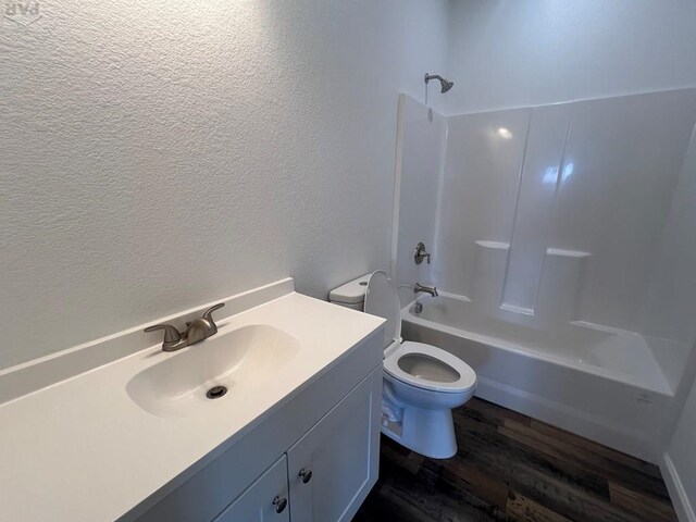 full bathroom with a textured wall, toilet, wood finished floors, vanity, and shower / bathing tub combination