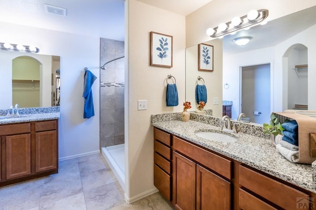 bathroom with two vanities, visible vents, tiled shower, and a sink