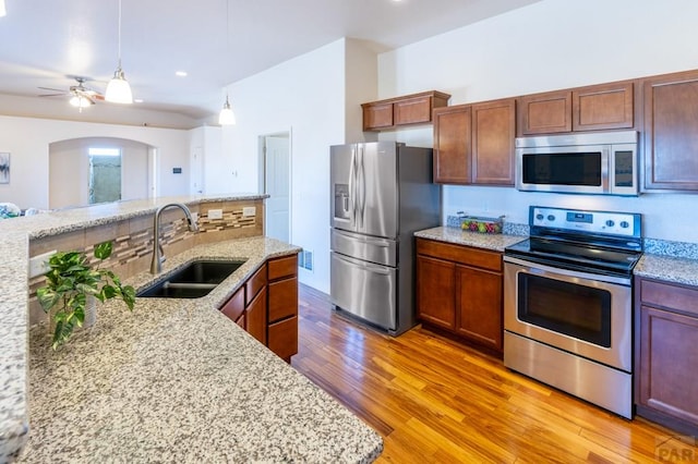 kitchen featuring a sink, light wood-style floors, decorative backsplash, a ceiling fan, and appliances with stainless steel finishes