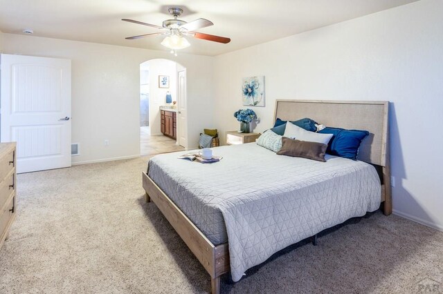 bedroom featuring a ceiling fan, light carpet, connected bathroom, arched walkways, and baseboards