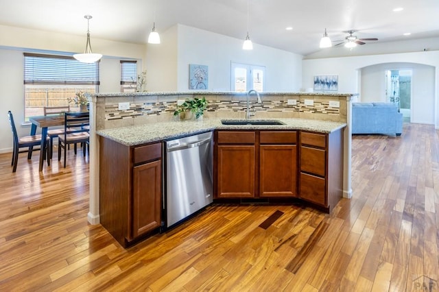 kitchen with backsplash, dishwasher, a sink, arched walkways, and brown cabinetry
