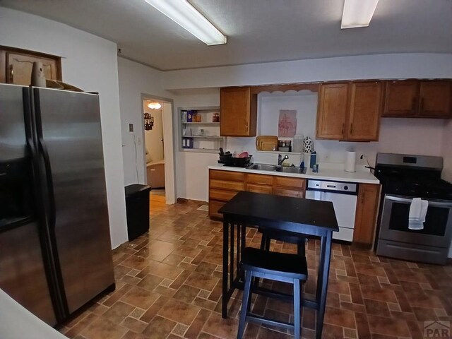 kitchen with a sink, light countertops, appliances with stainless steel finishes, brown cabinets, and stone finish floor